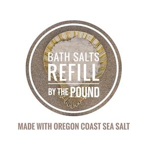 May include: A circular graphic with the words "BATH SALTS REFILL BY THE POUND" in white text. The text is inside a brown circle with a gold-colored decorative dish filled with white bath salts. The text "MADE WITH OREGON COAST SEA SALT" is below.
