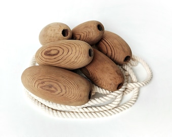 May include: A set of six wooden buoys with a natural wood finish, tied together with a white rope. The buoys are oval-shaped and have a smooth, polished surface.