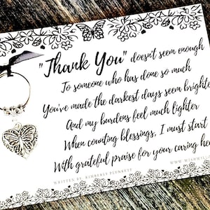 May include: A white card with a black floral border and the text "Thank You" in black script. A silver-colored heart-shaped charm with a butterfly design hangs from a keyring with a black ribbon.