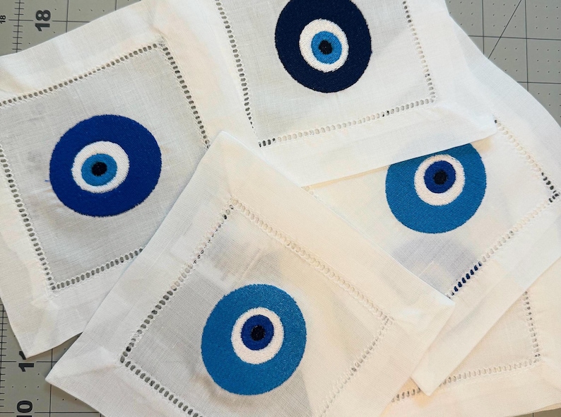 May include: Set of four white linen napkins with blue and white embroidered evil eye designs.