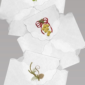 May include: Three white scalloped edge fabric napkins with embroidered Christmas designs. The first napkin has a green mistletoe with a red bow. The second napkin has a red bow with gold bells. The third napkin has a green pine branch with a pine cone and the letter "S".