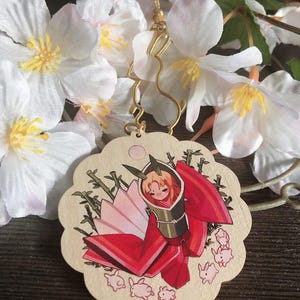 May include: A wooden charm featuring a hand-painted illustration of a woman in a red and white kimono with a bamboo background. The charm is surrounded by small pink rabbits.
