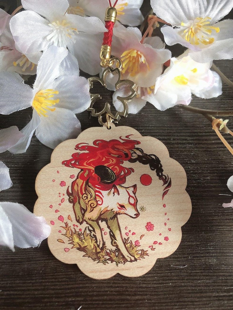 May include: A wooden charm featuring a red and white fox with a red flame tail, surrounded by pink cherry blossoms. The charm is attached to a red string with a gold cherry blossom charm.
