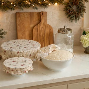 May include: Three fabric bowl covers featuring a cream background with a delicate floral pattern in shades of red, green, and brown. Two covers are fitted over bowls, while one is partially removed to reveal dough inside a white ceramic bowl.