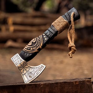 May include: A black and silver axe with a wooden handle wrapped in twine. The axe head has intricate carvings and runes. The handle is decorated with a knotwork design.