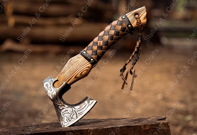 K&ouml;nnte beinhalten: Eine handgeschmiedete Axt mit einem Holzstiel, der mit Leder umwickelt ist. Die Axtkopf hat ein detailliertes Design und der Stiel ist mit einem Lederriemen befestigt. Die Axt liegt auf einer Holzoberfl&auml;che.