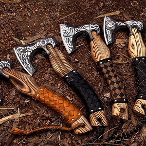 K&ouml;nnte beinhalten: F&uuml;nf handgeschmiedete &Auml;xte mit Holzstielen und Lederummantelungen. Die &Auml;xte haben aufwendige Designs und Muster, die in das Metall einge&auml;tzt sind. Die Stiele sind aus verschiedenen Holzarten gefertigt und haben eine Vielzahl von Lederummantelungen.
