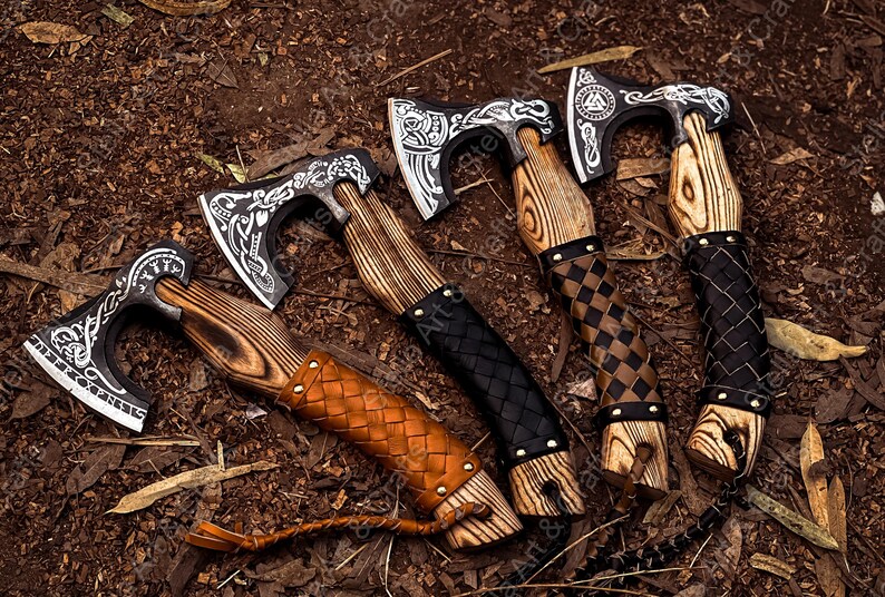 K&ouml;nnte beinhalten: F&uuml;nf handgeschmiedete &Auml;xte mit Holzstielen und Lederummantelungen. Die &Auml;xte haben aufwendige Designs und Muster, die in das Metall einge&auml;tzt sind. Die Stiele sind aus verschiedenen Holzarten gefertigt und haben eine Vielzahl von Lederummantelungen.