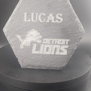 May include: A gray hexagonal slate coaster with the Detroit Lions logo and the text "Lucas" and "DETROIT LIONS" engraved on it.