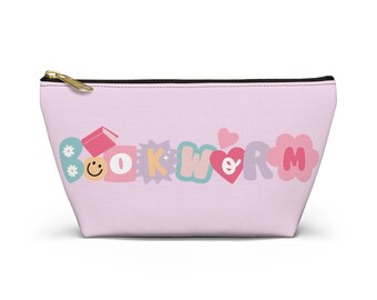 Op de afbeelding: Een lichtroze etui met rits voorzien van het woord BOOKWORM in kleurrijke, gestileerde letters. Het ontwerp bevat een klein boekje, een smiley, een ster en hartvormen die in de letters zijn verwerkt, op een effen lichtroze achtergrond.