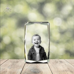 Op de afbeelding: Een kristallen kubus met een zwart-witfoto van een lachend kind erin. De kubus staat op een houten oppervlak.