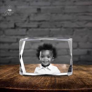 Op de afbeelding: Een kristallen kubus met een 3D-gegraveerd beeld van een jong kind met donker haar en een wit shirt. De kubus staat op een houten oppervlak.
