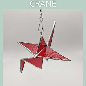 Op de afbeelding: Een rode origami-kraan van gekleurd glas, hangend aan een zilveren ketting. De kraan is een traditioneel Japans symbool voor vrede en geluk.