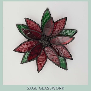 May include: A stained glass 3D poinsettia with red and green petals and black edging. The image includes the text "3D POINSETTIA" and "SAGE GLASSWORK".