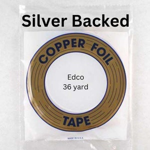 May include: A roll of gold-colored copper foil tape with the text "Copper Foil Tape" printed in black around the outside of the roll. The text "Edco 36 yard" is printed in black on a white background inside the roll. The roll is packaged in a clear plastic bag with the text "Silver Backed" printed in black at the top.