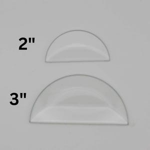 May include: Two white plastic half-circle cake decorating tools. The larger tool is 3 inches in diameter and the smaller tool is 2 inches in diameter.