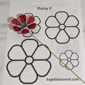 May include: A stained glass daisy flower with red petals and a purple center, mounted on a gold-colored metal stem. The image also shows a printed sheet with the text "Daisy 2" and flower outlines for a craft project.