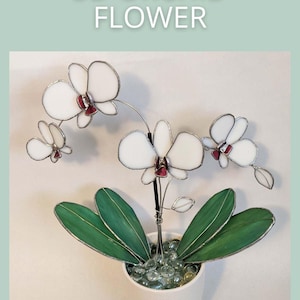 Può includere: Una scultura di fiori di orchidea in vetro 3D con petali bianchi e centri rossi, posta in un vaso bianco con foglie verdi e perle di vetro. Il testo "3D ORCHID FLOWER" è sopra la scultura.