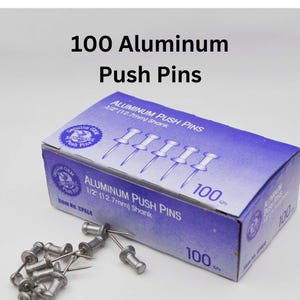 May include: A box of 100 silver aluminum push pins. The box is purple and blue with white text that reads "Aluminum Push Pins 1/2" (12.7mm) Shank" and "100 ct."