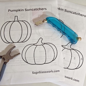 May include: Two sheets of paper with pumpkin outlines and the text "Pumpkin Suncatchers" and "SageGlasswork.com". A blue glass cutter and pliers are on the paper. The glass cutter is 6-19mm.