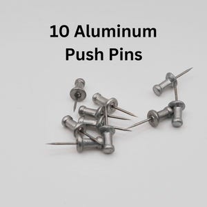 May include: A set of 10 silver aluminum push pins. The pins are scattered on a white surface.