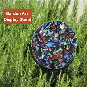May include: A round, colorful mosaic garden art piece on a black metal stand. The mosaic is made of small, broken pieces of glass and tile in various colors, including blue, green, red, and yellow. The stand is tall and slender, with a circular base. The art piece is displayed in a garden setting, surrounded by green plants.