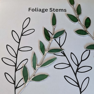 以下が含まれることがあります： 緑色のステンドグラスの葉の茎、銀色のハンダ付け、黒い葉の輪郭のある白い背景。上部には「Foliage Stems」の文字。これらの装飾的な茎は、あらゆるクラフトプロジェクトに自然のタッチを加えます。