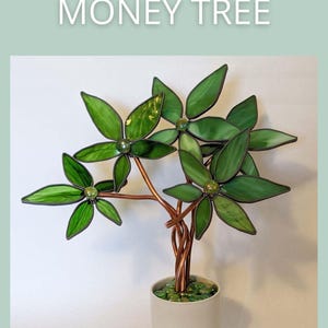 May include: A handcrafted glass money tree sculpture with green leaves and copper wire branches. The tree is in a white pot filled with green stones. The text "MONEY TREE" and "SAGE GLASSWORK" are displayed.
