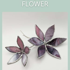 Peut inclure: Deux sculptures de fleurs de lys 3D en vitrail dans des tons de violet et de rose. Les fleurs ont des bordures et des tiges en métal argenté. Le texte "3D LILY FLOWER" est au-dessus des fleurs et "SAGE GLASSWORK" en dessous.