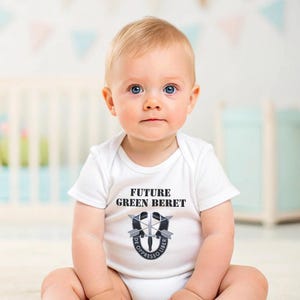May include: A white baby onesie with the text "FUTURE GREEN BERET" and a black and white emblem with the text "DE OPPRESSO LIBER".