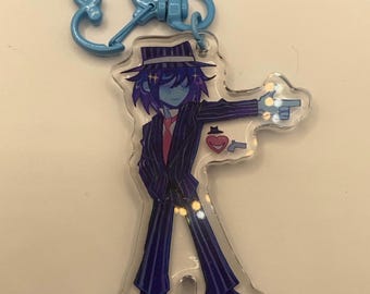 May include: A clear acrylic keychain featuring a cartoon character in a pinstripe suit, fedora, and red tie, pointing a finger gun. The keychain has a blue heart-shaped clasp.