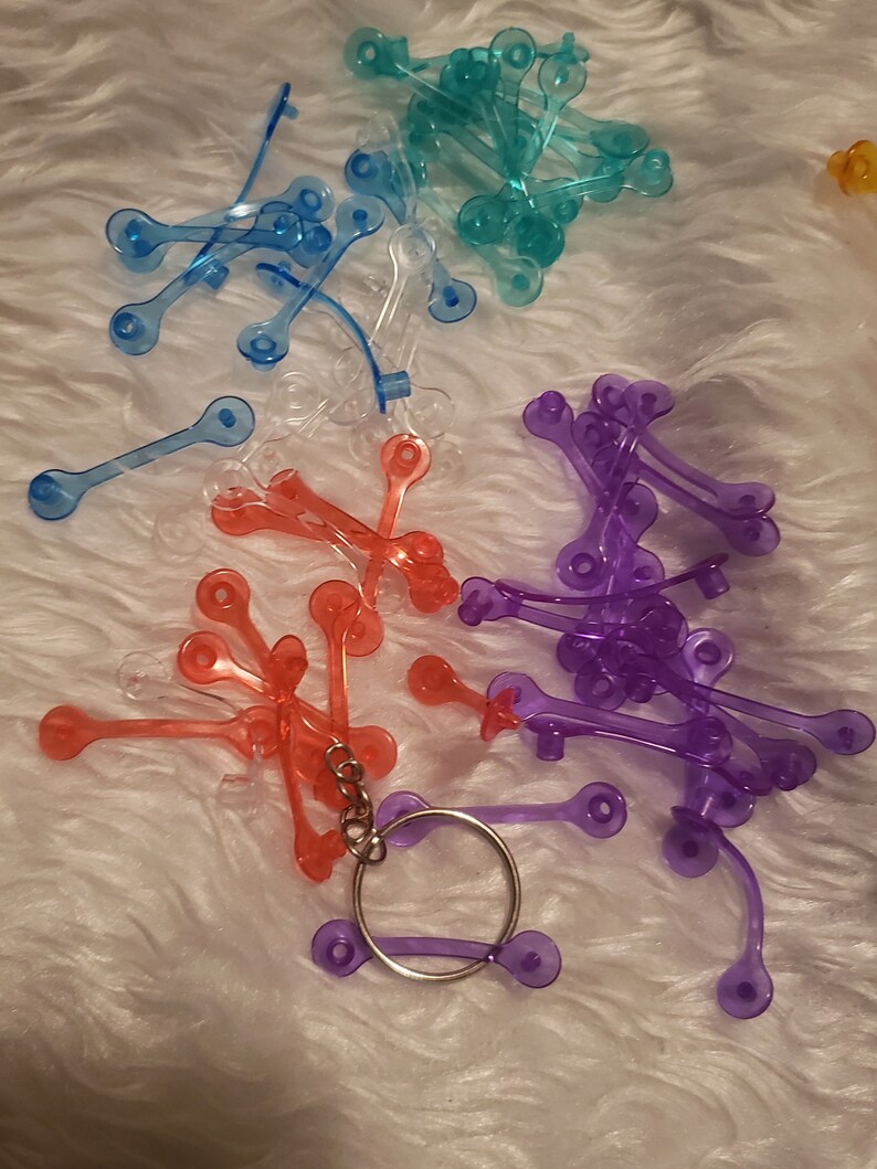 May include: Assortment of colourful plastic keychains in blue, purple, red, and clear. The keychains are shaped like a simple loop with two small circles on each end.