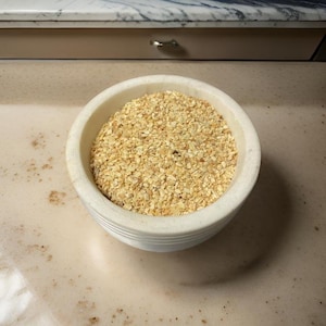 May include: A white ceramic bowl filled with finely chopped, light brown garlic.