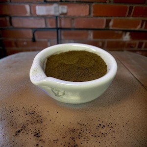 May include: A white ceramic mortar and pestle filled with a dark brown powder.