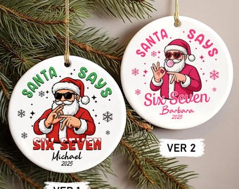 May include: Two white Christmas ornaments with gold string hangers. Each ornament features a cartoon Santa Claus wearing sunglasses and a red suit. The text "SANTA SAYS" and "SIX SEVEN" is printed on each ornament, along with a name and the year 2025.