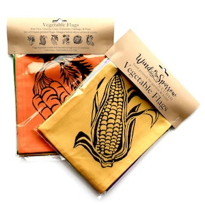 May include: Set of six hand-printed cotton flags featuring vegetables, including carrots, corn, bok choy, tomatoes, cabbage, and peas. The flags are packaged in a clear plastic bag with a brown paper header card that reads "Vegetable Flags" and "Wind Sparrow Studio".
