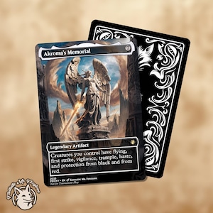 May include: A collectible card featuring "Akroma's Memorial" with a detailed illustration of an angel statue holding a sword. The card has a black border and text that reads "Legendary Artifact". A second card with a decorative black and white design is visible.