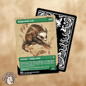 May include: A collectible card featuring a badger-like creature labeled "Badgermole Cub." The card has a tan background with a detailed illustration of the creature. A black card with white ornate designs is behind it. The text includes "Creature - Badger Mole" and "2/2."