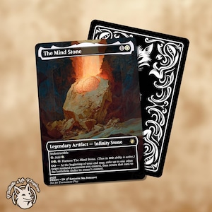 Può includere: Una carta fantasy intitolata "The Mind Stone" con un'illustrazione dettagliata di un oggetto luminoso a forma di cervello su una formazione rocciosa. La carta ha un bordo nero e il testo "Legendary Artifact - Infinity Stone". Una seconda carta con un design decorativo in bianco e nero è dietro.