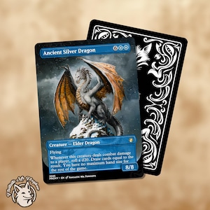 Puede incluir: Una carta de fantasía con un Dragón Plateado Antiguo con alas naranjas, posado sobre una roca nevada. La carta tiene un borde azul y el texto "Ancient Silver Dragon" y "Creature - Elder Dragon". Una carta negra con remolinos decorativos blancos está detrás.