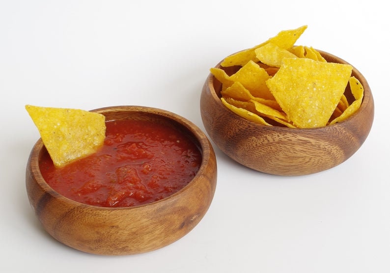 May include: Two wooden bowls, one filled with red salsa and a yellow tortilla chip, the other filled with yellow tortilla chips.