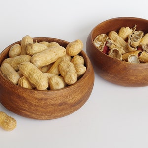 May include: Two wooden bowls filled with peanuts. One bowl contains whole peanuts, while the other bowl contains peanut shells.