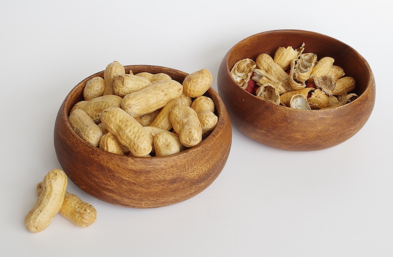 May include: Two wooden bowls filled with peanuts. One bowl contains whole peanuts, while the other bowl contains peanut shells.