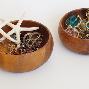 May include: Two wooden bowls, one filled with colorful glass beads and gold chains, the other with white starfish and assorted jewelry.
