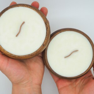 May include: Two wooden bowls with white candles and wooden wicks. The bowls are made of dark wood and have a natural finish.