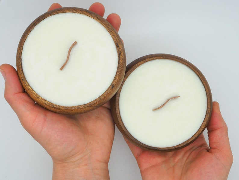 May include: Two wooden bowls with white candles and wooden wicks. The bowls are made of dark wood and have a natural finish.