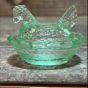 K&ouml;nnte beinhalten: Ein gr&uuml;nes Glas-Salz- und Pfefferstreuer-Set in Form eines Huhns. Das Huhn sitzt in einem Nest.