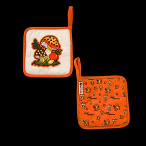 May include: Two square orange and white pot holders. One features a mushroom design with orange, yellow, and brown colors. The other has a repeating pattern of mushrooms and the text "Rustic Timber". Both have orange trim and a hanging loop.