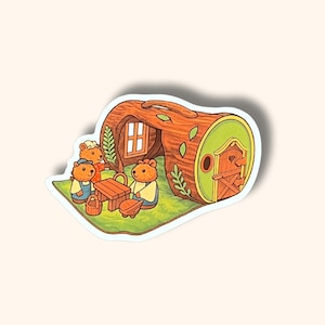 May include: A whimsical sticker featuring a cartoon scene of bears gathered around a table in front of a log cabin. The cabin has a green door and window. The bears are wearing clothes and there is a picnic basket and a small wagon.