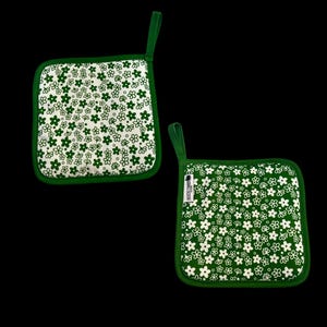 May include: Two square pot holders with a green floral pattern on a white background. The pot holders have a green border and a green loop for hanging. The pot holders are made of fabric.